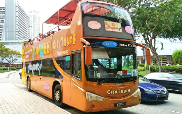 Vibrant FunVee bus, tourists aboard, traverses Singapore's streets, an exciting journey painted in bright orange and enthusiasm.